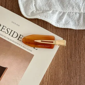 Detailed shot of a stylish brown acetate hair clip with gold metal bobby pin design.