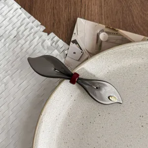 Detailed view of grey leaf spring hairpin with red bow accent and gold logo detail.