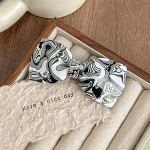 Detail shot of a French rhinestone bow hair clip with black white swirl acetate design.