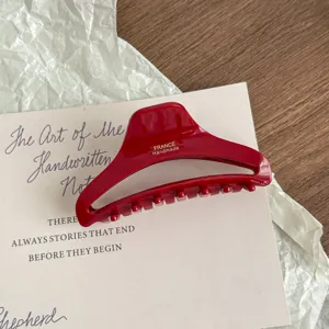 Close-up detail of the red acetate hair claw clip with golden lettering on wooden background.