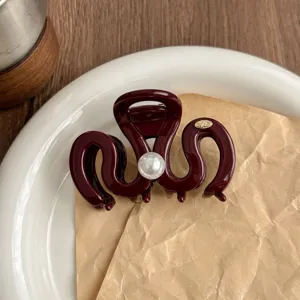 Detail view of dark red resin hair claw clip featuring a central pearl and metallic logo.