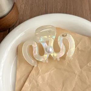 Close-up of iridescent hair claw clip featuring a shiny pearl and metallic logo detail.