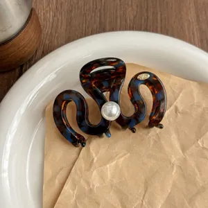 Detail shot of a brown tortoise shell hair claw clip featuring a chic center pearl accent.