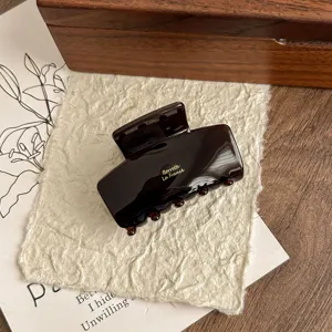 Detailed close-up of dark brown acetate hair claw clip, glossy shark clip with golden lettering.
