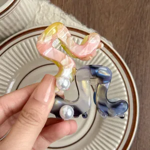 Close-up detail of stylish acetate hair claw clip with pearl accent and marbled pattern.