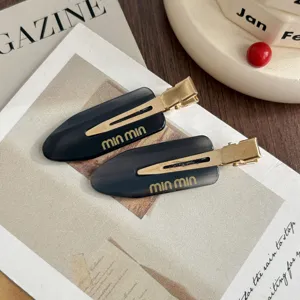 Close-up detail of sleek acetate hair clip with gold metal snap, stylish dark design.
