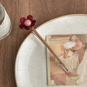 Primer plano de la horquilla floral rojo oscuro con perla rosa en plato decorativo.
