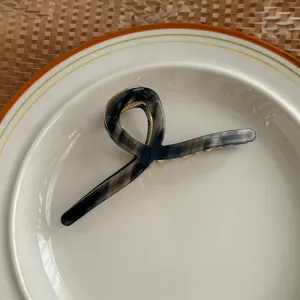 Elegant acetate hair claw clip with unique curved loop design and fine metallic details.