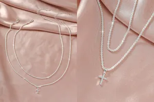 Gedetailleerd close-up van de sprankelende dubbellaagse zilveren ketting met kruis op satijn.