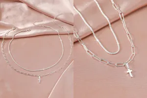 Dubbele zilveren ketting met kruis hangertje en glimmende ketting op roze satijn.