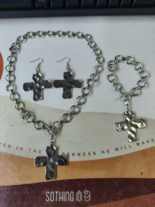 Detailed view of metal cross pendant necklace, earrings, and bracelet jewelry set.