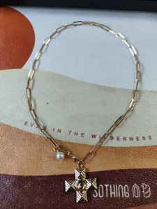 Gold paperclip chain necklace with pearl charm and detailed cross pendant for women fashion.