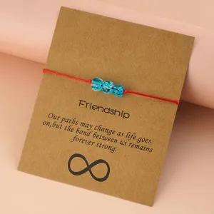 Handmade red braided cord bracelet with three blue glass beads on a kraft paper card.