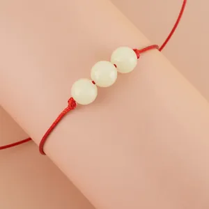 Handmade red woven rope bracelet with three white luminous beads, elegant wristwear detail.