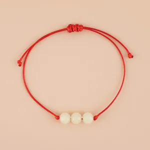 Close up detail of handmade red string woven bracelet featuring three smooth white beads and knot.