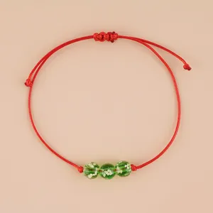 Detailed view of handmade red braided cord bracelet featuring three green luminous glass beads.