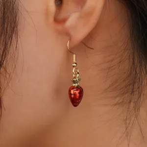 Primo piano dettaglio di orecchini pendenti fragola rossa indossati, accessorio chic.