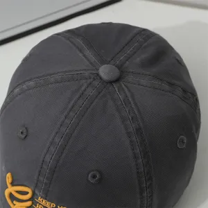 Dark grey baseball cap top detail, soft crown structure with yellow embroidery letters.