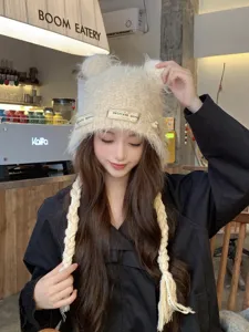 Detail view of a cute beige knitted beanie hat with bear ears and braided tassel strings.