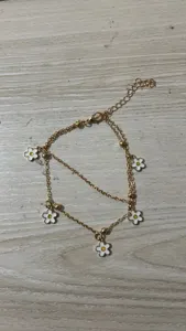 Detail shot of the double-layer gold chain anklet featuring delicate white enamel flower charms.