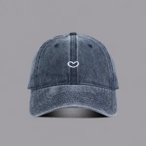 Closeup of washed denim baseball cap with cute white heart embroidery detail and curved brim.