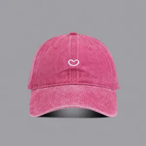 Close-up view of the washed pink baseball cap featuring a delicate white embroidered heart.