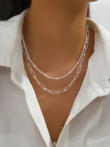 Close-up view of a double layer silver sparkling and paperclip chain necklace on white shirt.