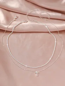 Elegant double layer silver necklace with a tiny cross pendant on pink satin background.