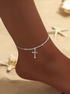 Detailaufnahme einer silbernen Strass-Kreuz-Fußkette am Sandstrand, funkelnder Sommerschmuck.