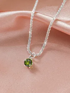 Detail shot of a sparkling green gemstone pendant necklace on pink silk, elegant clavicle chain.