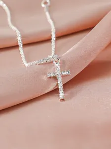 Nahaufnahme eines glitzernden Strass-Kreuzanhängers auf weichem rosa Satinhintergrund.