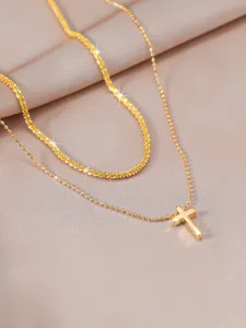 Close-up detail of double layer gold necklace featuring a delicate cross pendant on fabric.