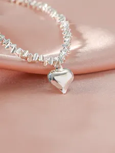 Detaillierte Nahaufnahme einer schimmernden silbernen Perlenkette mit poliertem Herzanhänger.