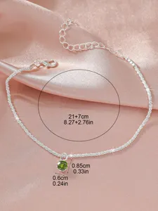 Minimalistische Silberfußkette mit funkelndem grünem Steinanhänger, eleganter Strandschmuck.
