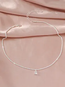 Detail shot of a sparkling silver clavicle chain with rectangular pendant on pink background.