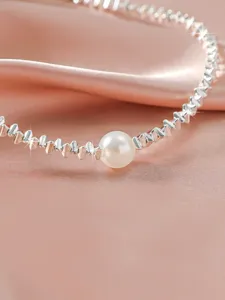 Elegant silver textured chain necklace with central pearl on pink silk fabric background.