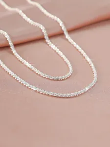 Sparkly silver chain necklace detail shot on pink satin background, elegant jewelry close-up.