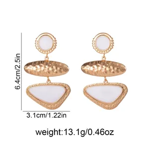 Detailed view of long geometric oval gold earrings with white enamel accent and metal finish.