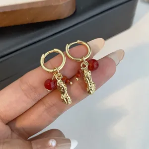 Close-up of gold-plated huggie hoop earrings with cute peanut pendant and red beads.