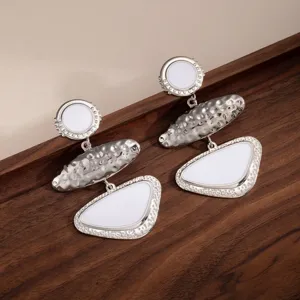 Detailed shot of retro geometric metal drop earrings with white enamel and silver finish.