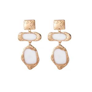 Boucles d'oreilles pendantes géométriques dorées avec émail blanc, style rétro élégant.