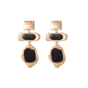 Gros plan de boucles d'oreilles pendantes rétro géométriques dorées avec détails en émail noir.