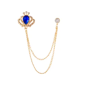 Detailed shot of gold-toned crown brooch with blue teardrop crystal and double hanging chains.