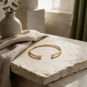 Detalle de brazalete abierto de metal dorada minimalista con suaves curvas geométricas.