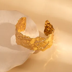 Close-up of wide textured irregular gold metal open cuff bracelet, unique retro design detail.