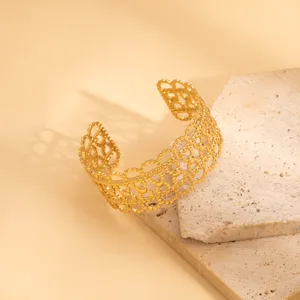 Detail view of a wide gold open cuff bracelet with intricate geometric hollow design.