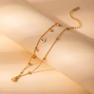 Detailed view of gold stainless steel layered charm bracelet with crystal and pendants.