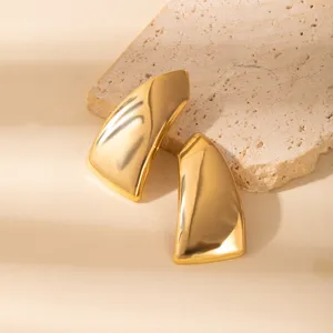Close-up detail of vintage style gold geometric leaf earrings on textured stone backdrop.