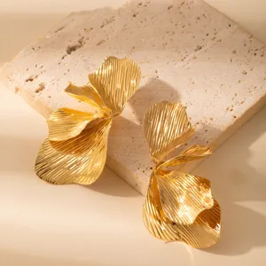 Close-up detail of oversized gold leaf earrings, featuring textured metallic floral design.