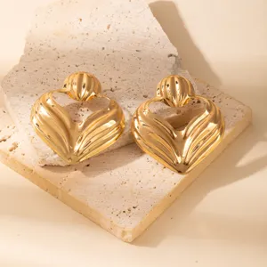 Close-up detail of luxurious gold hollow leaf geometric earrings on stone prop. Elegant design.